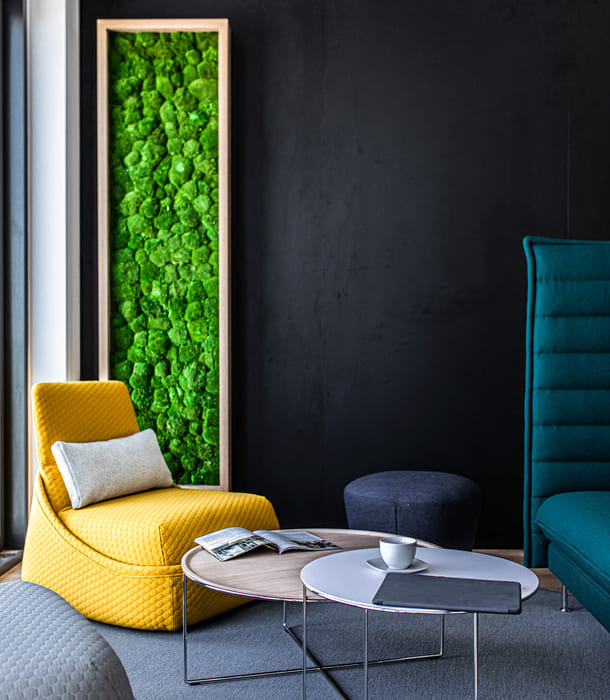 Modern eingerichteter Büroraum mit gelbem Sessel, rundem Tisch und vertikaler Begrünung an der Wand.